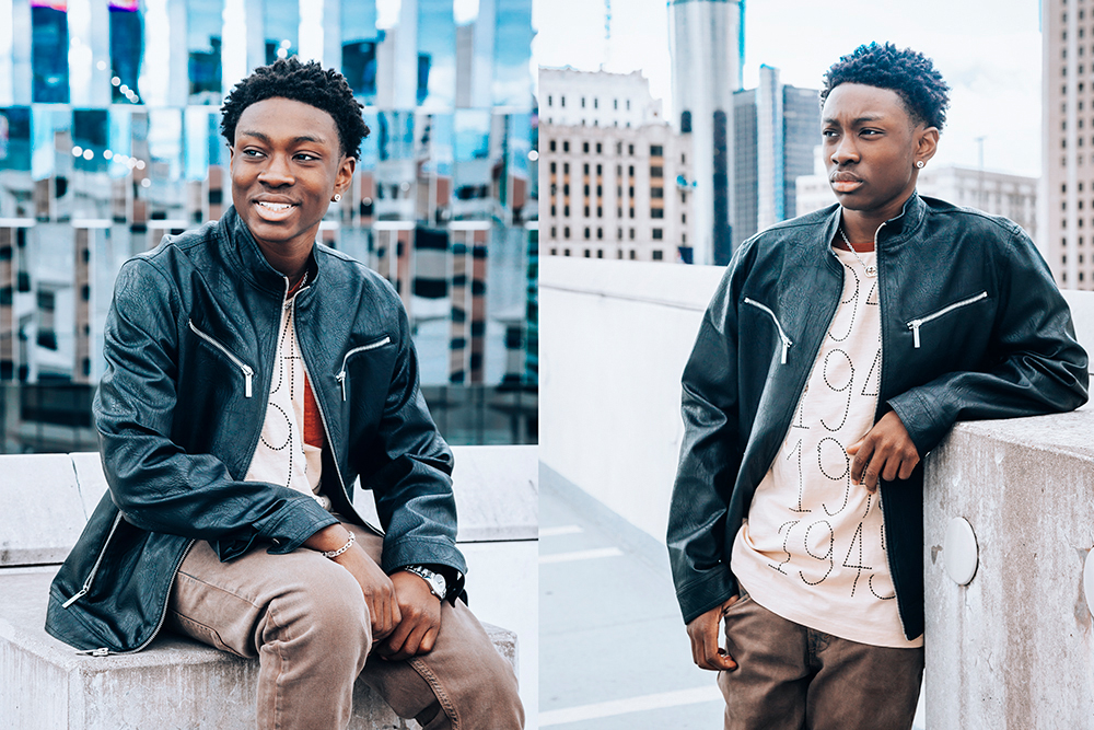 Two images of a person with short hair, wearing a black leather jacket and light-colored shirt with numbers. In the first image, they are sitting and smiling. In the second, they are standing by a wall on a rooftop, looking to the side. Urban background.