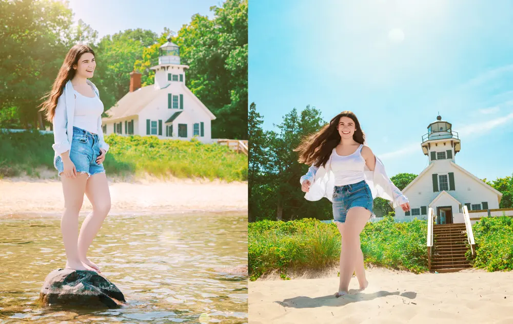 High school senior in denim shorts and white top enjoys a sunny day at the beach near a white lighthouse on Old Mission Peninsula. She stands on a rock in the water and walks on the sand, with green trees and a clear sky in the background.