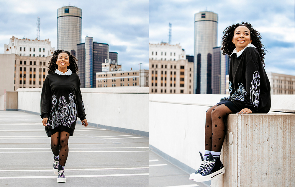 A person with curly hair is on a rooftop, wearing a black dress with white designs and black polka dot tights. They are shown walking and sitting, smiling against a cityscape background with tall buildings.