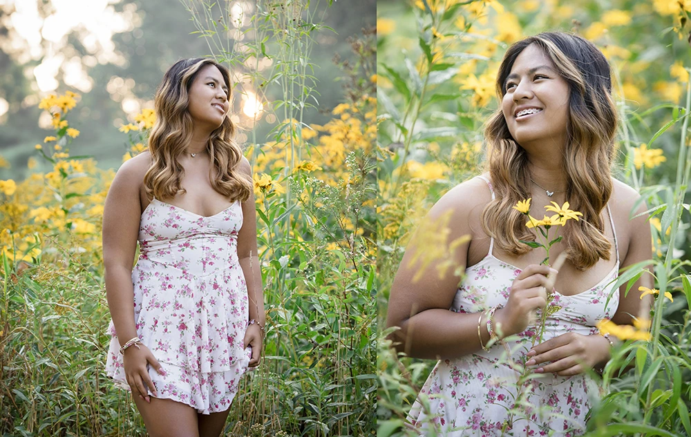 A high school senior girl in a white floral dress stands in a field of tall yellow flowers, smiling and enjoying the natural surroundings during her Nichols Arboretum senior pictures session in soft, golden sunlight.