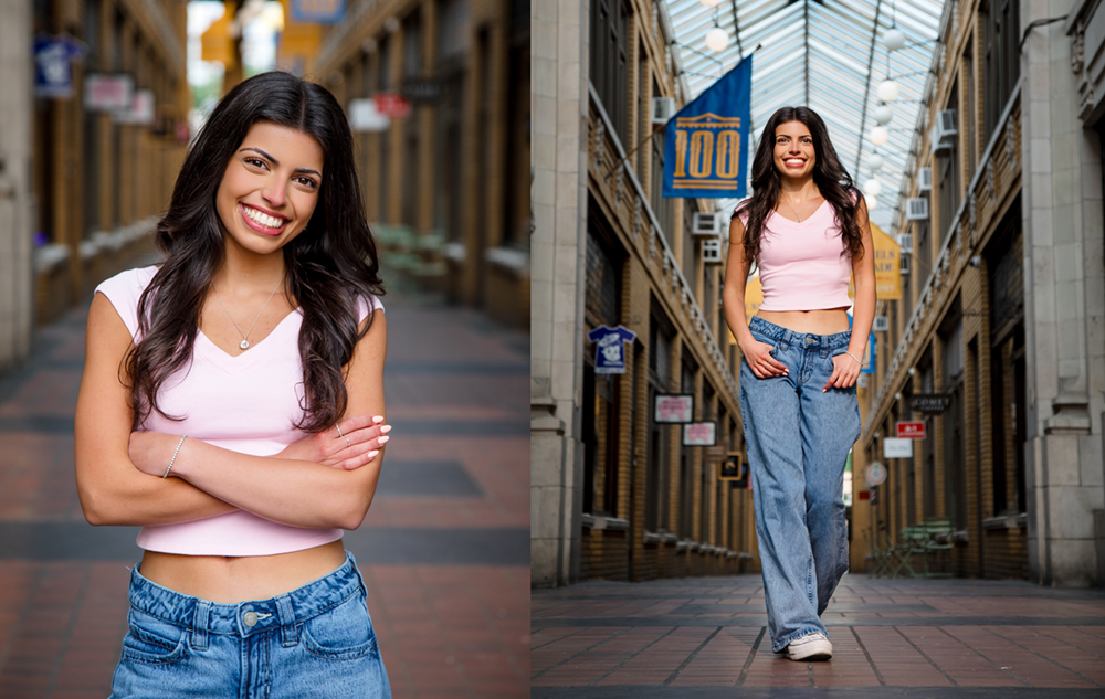 A young woman with long dark hair, wearing a light pink top and blue jeans, stands and smiles in an indoor arcade with high glass ceilings and decorative banners—perfect inspiration for unique senior pictures with flowers or urban charm.