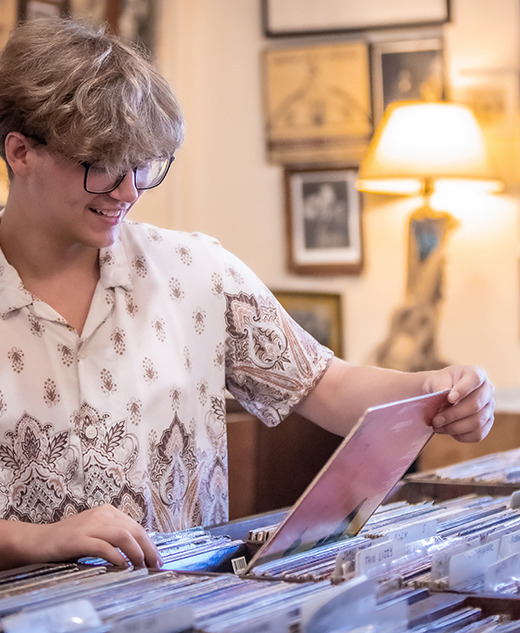 A high school senior browses through vinyl records for their senior pictures session in a cozy, vintage record store filled with framed photos.