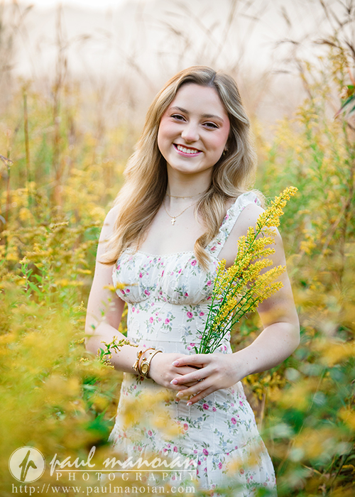 A high school senior girl holding a bouquet of yellow flowers during her Novi senior pictures session.