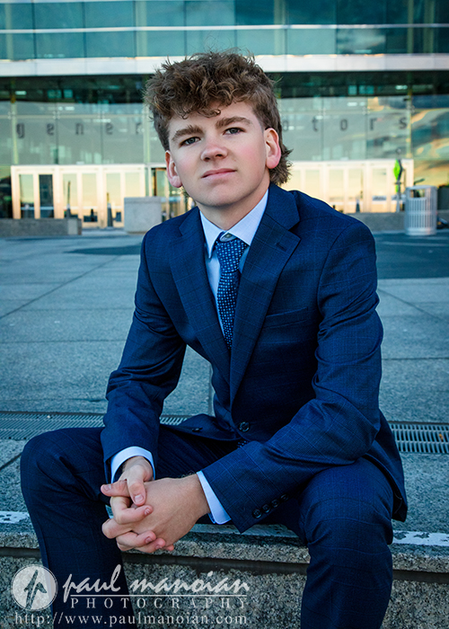 A man in a suit sits on the ground during a session for Northville senior pictures in downtown Detroit.