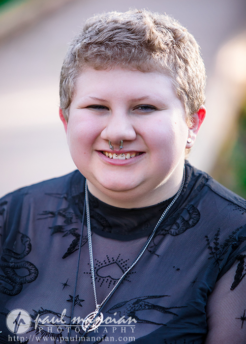 Smiling person with short hair and nose piercing, wearing a black top and necklace, outdoors in Ann Arbor—capturing true personality for senior pictures.