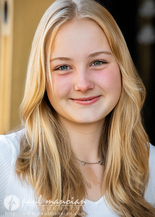 Teen girl with long blonde hair smiling, wearing a white top, standing in soft natural light—perfect for Ann Arbor senior pictures.
