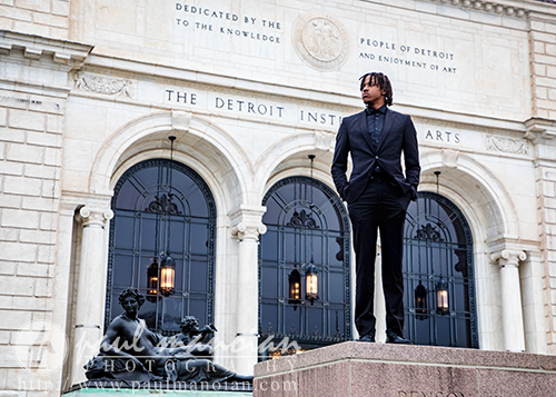 A high school senior in a black suit stands confidently in front of the Detroit Institute of Arts building, capturing stylish senior pictures Detroit.