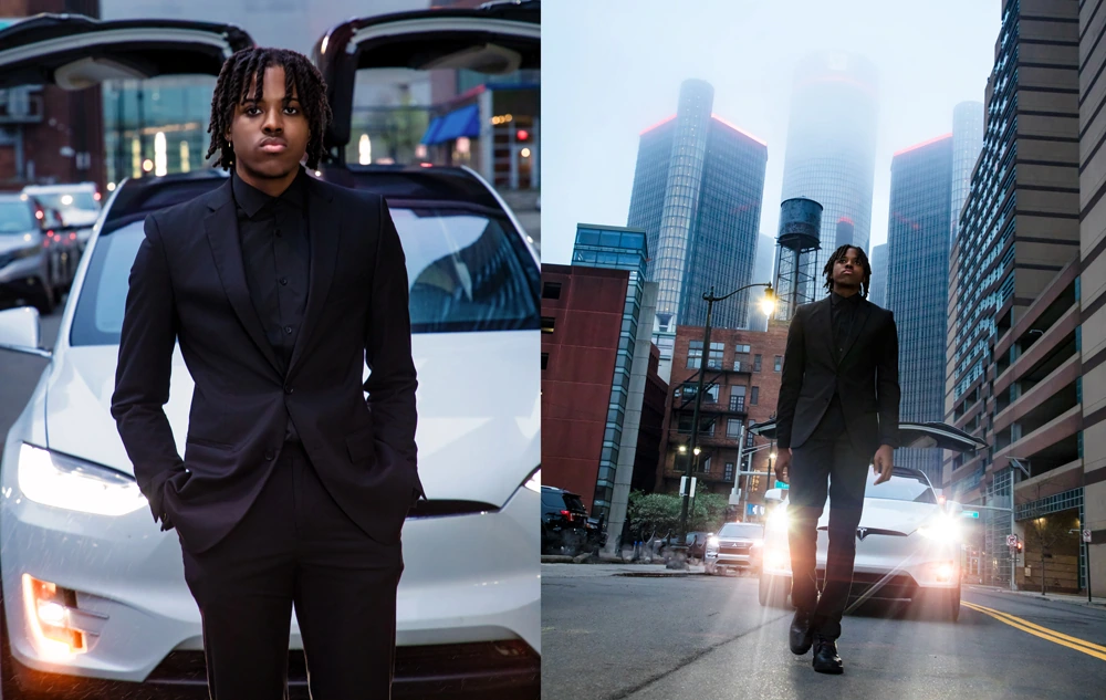 A high school senior in a black suit stands in front of a white Tesla with open doors, capturing the an editorial vibe for his downtown Detroit senior pictures session.