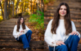 A young woman with long brown hair, wearing a white sweater and blue jeans, sits on outdoor steps covered with autumn leaves during her fall senior pictures session. Trees with colorful foliage are in the background. She is smiling in both images.