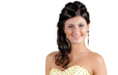 A woman with long dark hair styled in loose curls, wearing a strapless yellow dress with black polka dots and large dangling earrings, is smiling against a white background—perfect for pageant headshots.