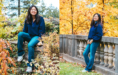 A young woman with long dark hair, wearing a blue sweater and jeans, poses outdoors among autumn foliage. In one photo, she sits on a stone ledge; in the other, she stands by a stone railing, both with a cheerful expression.