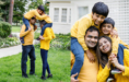A happy family of four, all wearing yellow tops, play outside. On the left, the parents smile as their two young sons climb on their backs. On the right, the family poses closely together, smiling at the camera.