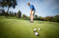 A golfer putts on a green with three golf balls near the hole on a sunny day, capturing the perfect moment for golf senior pictures.