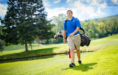 A high school senior walks on a sunny golf course carrying a golf bag over his shoulder, capturing the perfect moment for golf senior pictures.