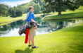 A man with sunglasses carries a golf bag by a pond on a green golf course, creating the perfect setting for timeless golf senior pictures.