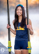A high school senior in a navy blue athletic outfit with SALINE in yellow poses outdoors for her senior pictures, holding two long oars. With long dark hair and a smile beneath her sunglasses, she captures the essence of the rowing crew against a blurred waterfront backdrop.