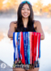 A high school senior, part of the rowing crew team, stands outdoors holding numerous medals with colorful ribbons. She wears sunglasses on her head and smiles at the camera. The blurred background of water and trees complements her vibrant spirit in these senior pictures.
