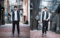 A young man in a black puffer vest, white hoodie, and black pants is standing and walking in an urban alley. The setting features brick and modern architecture, with outdoor lights and an overhead clock on the brick wall.
