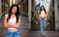 A high school senior girl with long dark hair, wearing a light pink top and blue jeans, stands and smiles in an indoor arcade with high glass ceilings and decorative banners—perfect inspiration for unique senior pictures with flowers or urban charm.