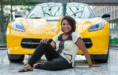 Smiling high school senior sits on marble floor in front of a bright yellow Corvette.